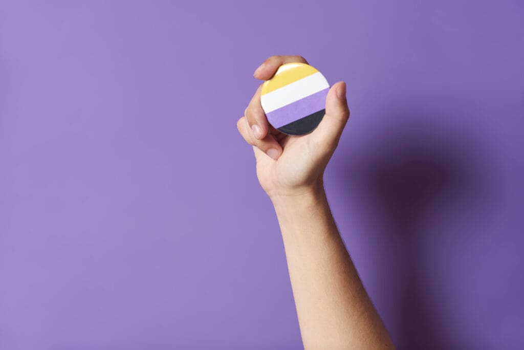 Hand holding nonbinary pride symbol representing inclusive gender affirming permanent makeup and identity aligned cosmetic tattooing available to clients across the United States