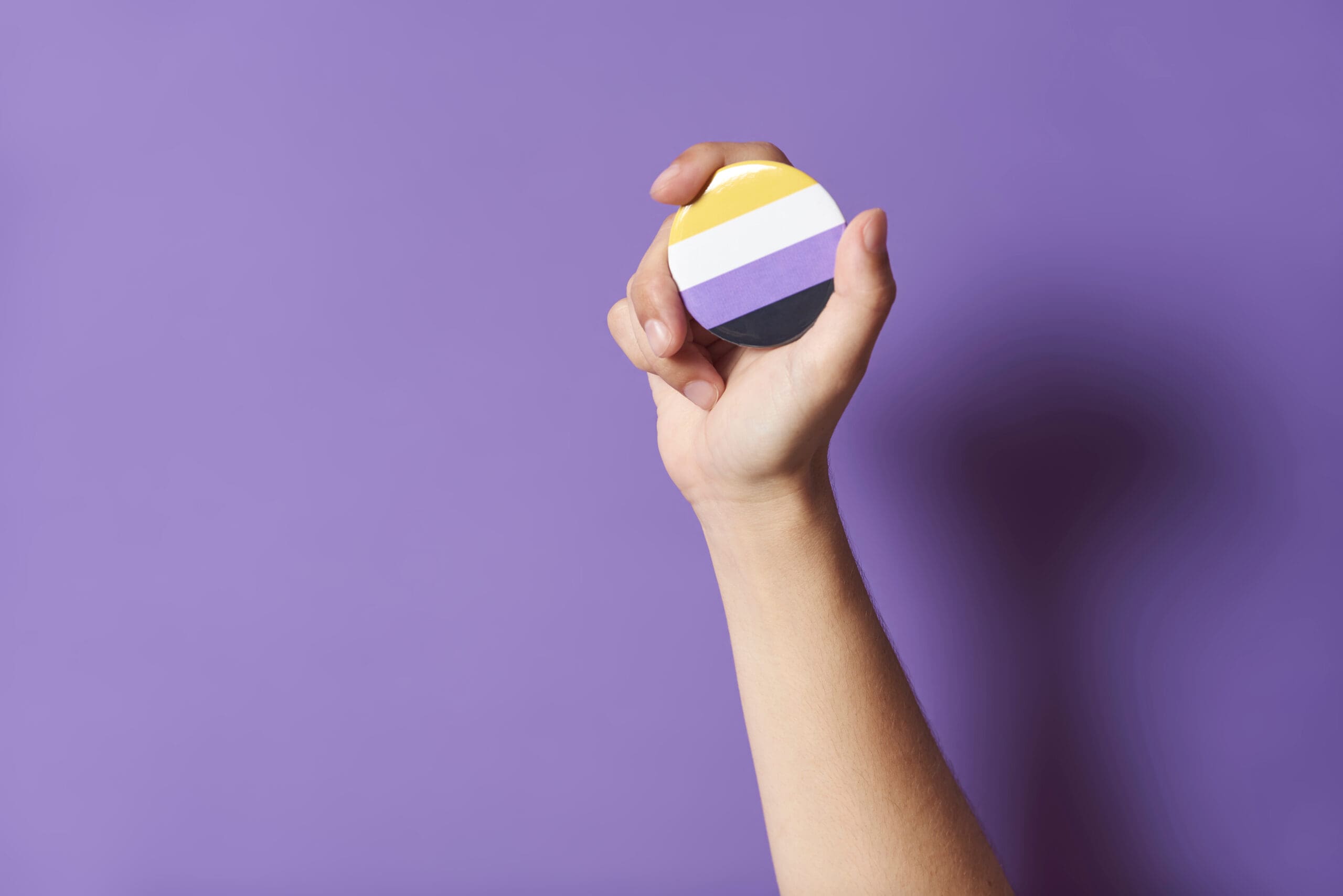 Hand holding nonbinary pride symbol representing inclusive gender affirming permanent makeup and identity aligned cosmetic tattooing available to clients across the United States performed by Salt Lake City Utah PMU Artist