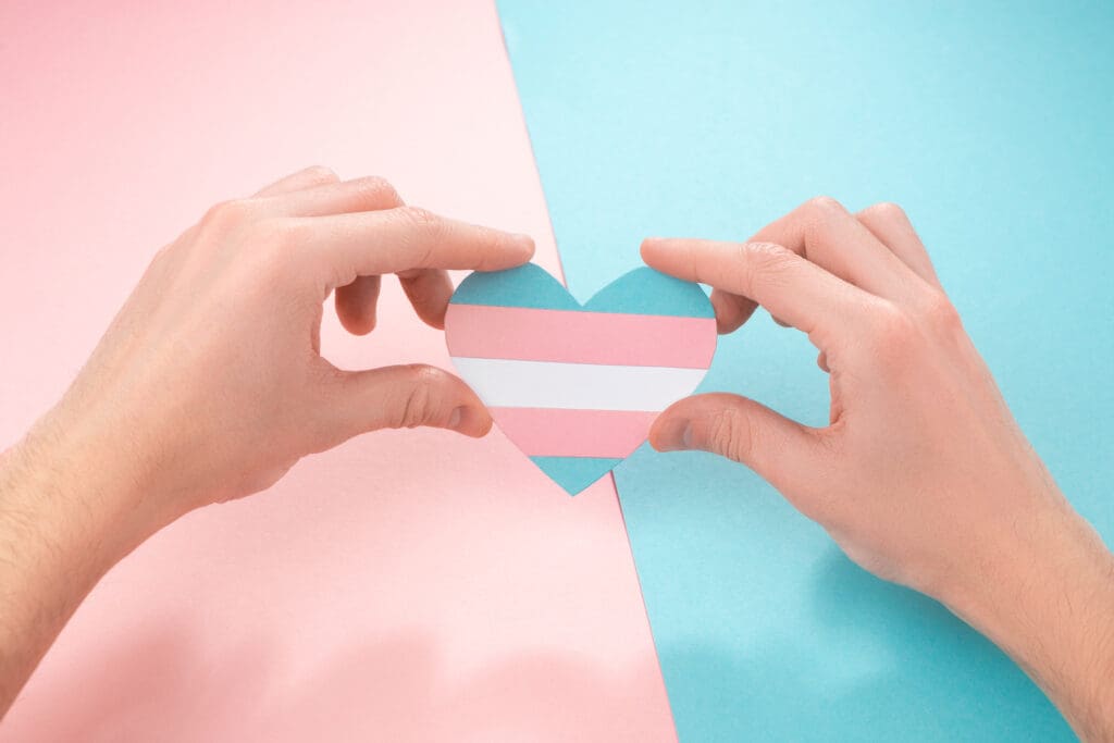 Hands holding transgender pride heart symbol representing gender affirming permanent makeup services and inclusive cosmetic tattooing support throughout the United States